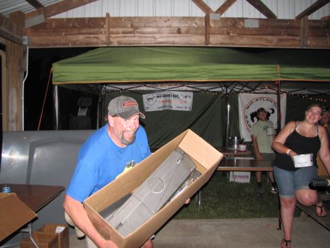 1979 Ford Bronco - Man holding a car part in a box at an outdoor event with tents and people.