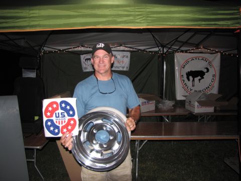 1979 Ford Bronco - A man displays a wheel and a sticker at an event with banners for 'Early Broncos'.