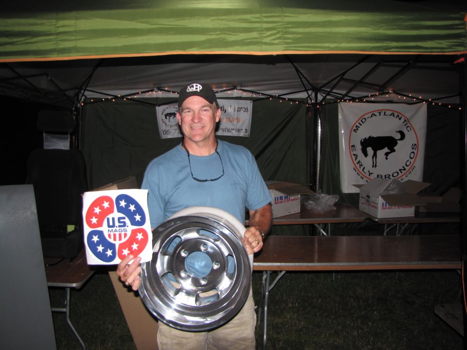 Man holds a shiny metal wheel and a sticker with red and blue stars and 'U.S. MAGS'