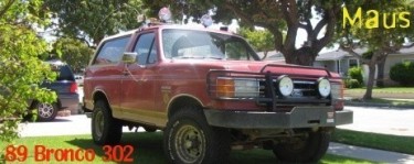 1989 Ford Bronco - A red 1989 Ford Bronco is parked on a grassy lawn in front of a residential street.