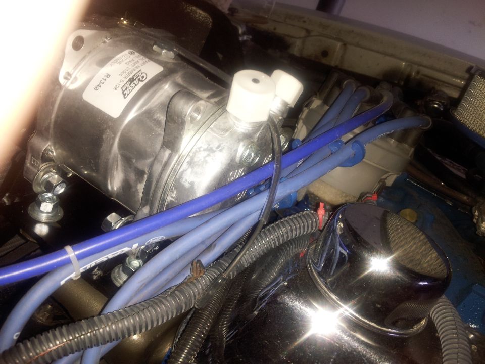 Close-up of an engine bay showing an air conditioning compressor and blue spark plug wires