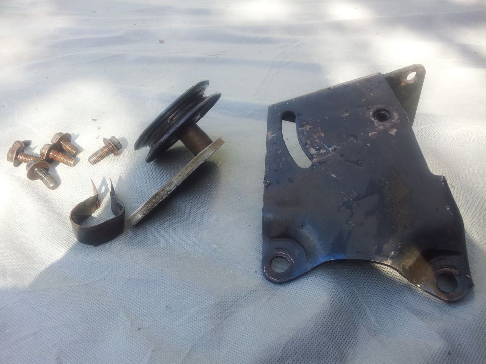 Air conditioning compressor bracket, pulley, bolts, and clamp on a light-colored surface