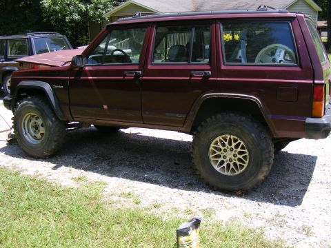 Maroon Jeep Cherokee XJ with aftermarket wheels and tires, parked next to another Jeep