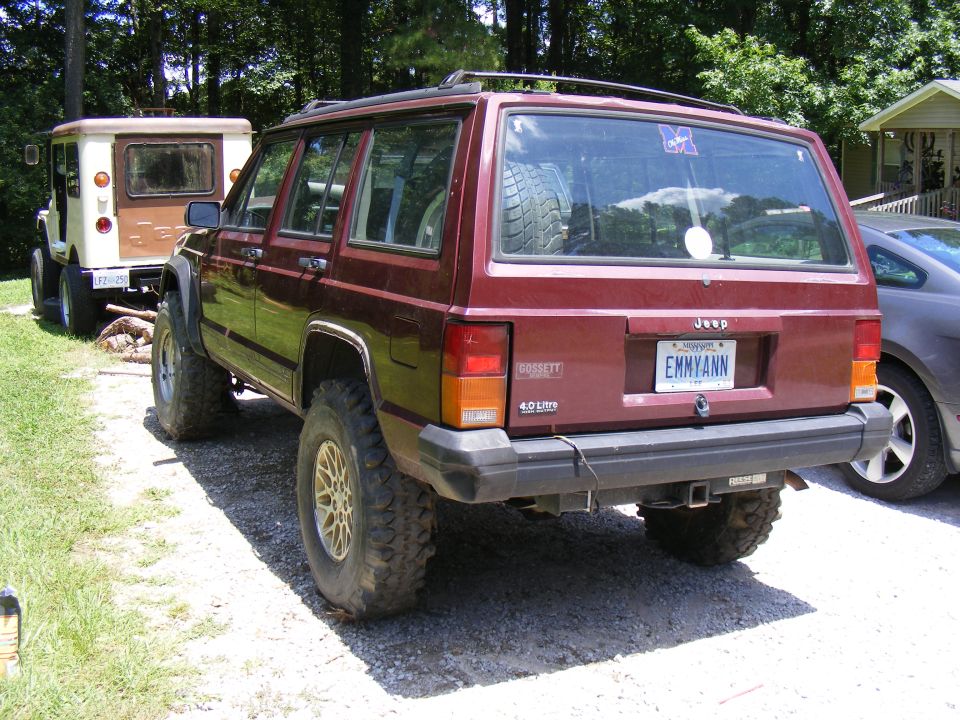 Maroon Jeep Cherokee XJ with lifted suspension and off-road tires. Another older Jeep is parked behind it