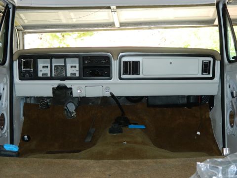 1979 Ford Bronco - Stripped cab interior of a Ford truck with two-tone dash, radio, vents, manual transmission shifter and brown carpet.