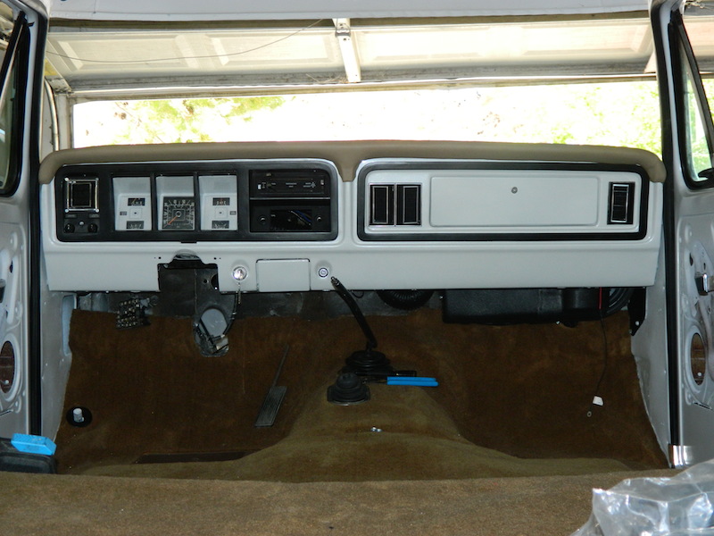 Bare interior of Ford truck showing tan dash, manual shifter and carpet