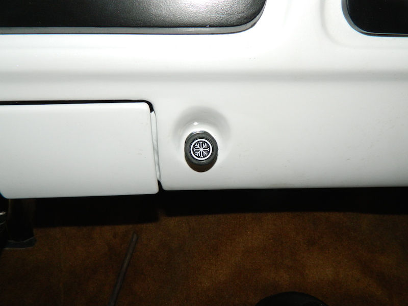 Close-up of a round black and white air conditioning control knob with a snowflake symbol on a white dashboard