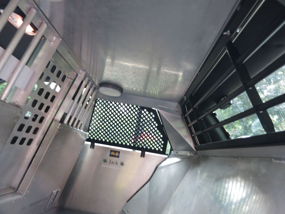 Interior of a K-9 transport vehicle with metal walls, grates, and a light. Text reads 'K-9 Jack'