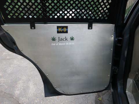 2001 Ford Crown Victoria - The interior of a police vehicle shows a K-9 decal and memorial text on a metal door panel.