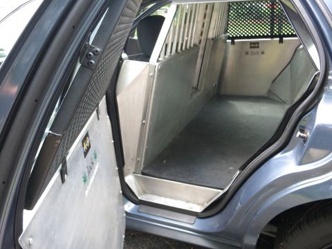 2001 Ford Crown Victoria - The interior of a blue police car is shown, modified for K-9 unit use with a metal cage and reinforced door panels.