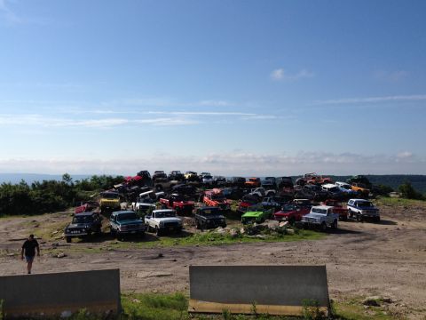 1988 Ford Bronco - A large collection of SUVs and trucks are parked on a hill, with a person walking in the foreground.