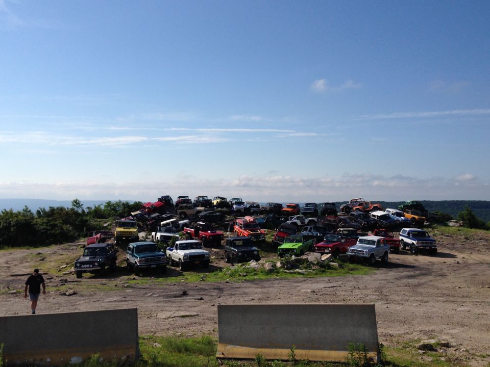 Junkyard scene with dozens of SUVs and trucks piled on a hill under a blue sky