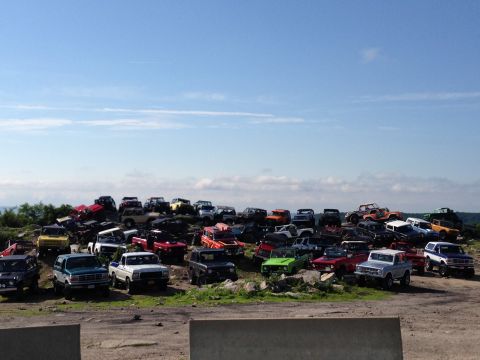 1988 Ford Bronco - A large collection of SUVs and trucks are parked on a grassy hill under a clear blue sky.