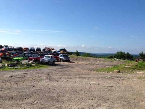 1988 Ford Bronco - A collection of vehicles sits in a junkyard under a clear blue sky.