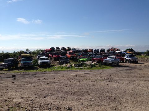 1988 Ford Bronco - A large collection of trucks and SUVs are parked on a grassy hill under a clear blue sky.