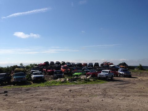 1988 Ford Bronco - A large collection of various trucks and SUVs are parked in a junkyard.