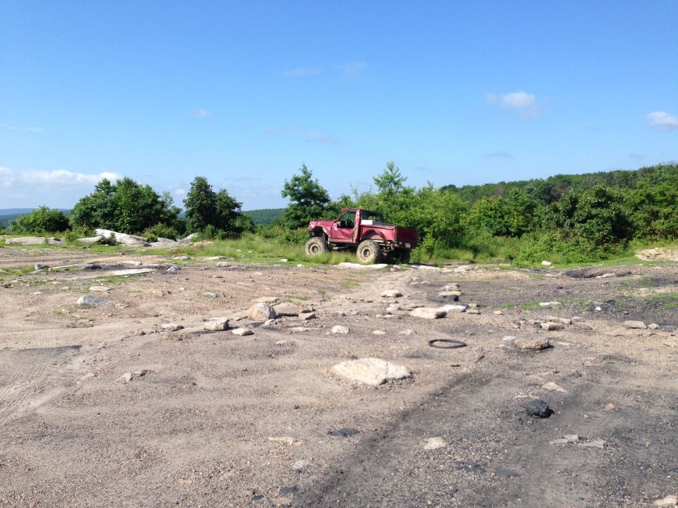 red pickup truck with large tires parked on rocky terrain with trees in background