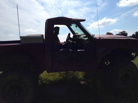1988 Ford Bronco - Red pickup truck with lifted suspension and off-road tires, driver in cabin. Text on fender reads 'RANGER 7.3'.