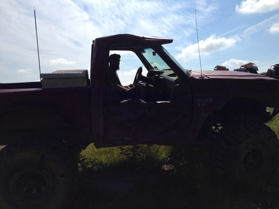 Side view of a red pickup truck with lifted suspension, driver visible inside. Text on fender reads 'RANGER 7.3'