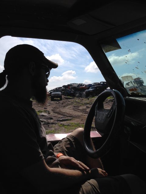 1988 Ford Bronco - View from inside a vehicle looking out at a junkyard filled with many cars under a cloudy sky.