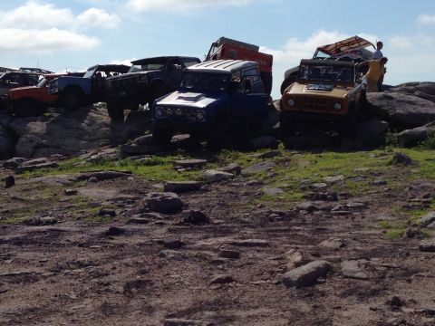 1988 Ford Bronco - Several off-road vehicles are parked on a rocky incline under a partly cloudy sky.