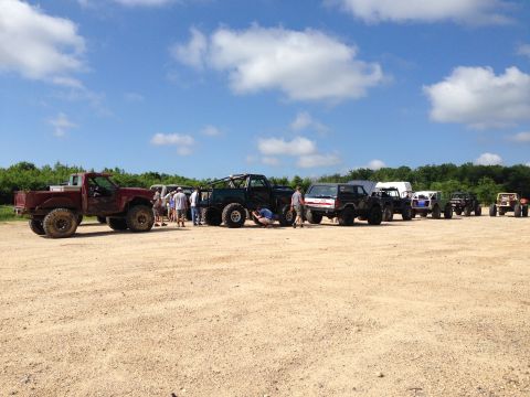 1988 Ford Bronco - Multiple off-road vehicles gathered in a dirt lot under a partly cloudy sky.