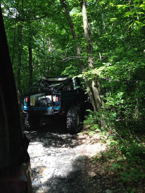 1988 Ford Bronco - Modified 1988 Ford Bronco navigating a challenging off-road path through dense woods.