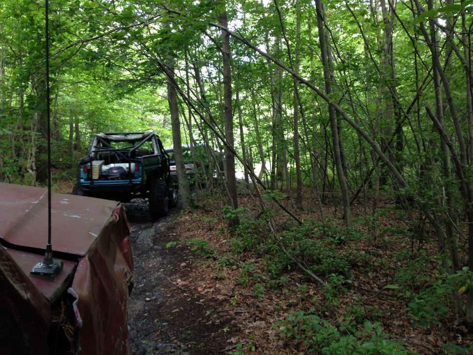 Two off-road vehicles driving on a muddy trail through a dense forest