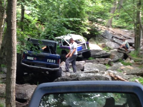 1988 Ford Bronco - Two off-road vehicles navigate a rocky trail in a wooded area.