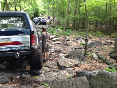 1988 Ford Bronco - Ford Bronco navigating a rocky off-road trail with other vehicles visible ahead.