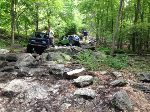 1988 Ford Bronco - Two off-road vehicles navigate a challenging rocky trail through a dense forest.