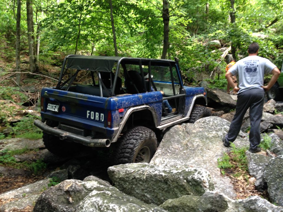 Blue 1988 Ford Bronco off-roading over rocks, rear view