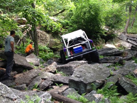 1988 Ford Bronco - A modified off-road vehicle tackles a challenging rocky path in a wooded area.