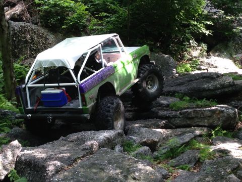 1988 Ford Bronco - An off-road vehicle with a custom canopy and roll cage tackles a challenging rocky trail.