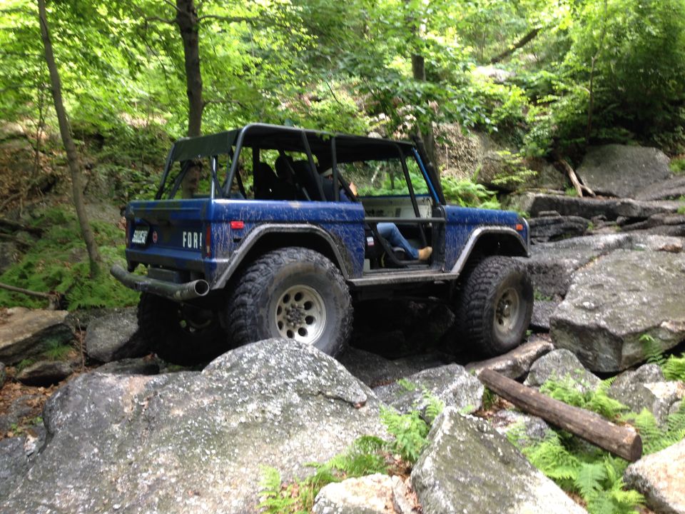 Blue SUV with roll cage driving over rocks on a trail. Has 'FORI' on the side
