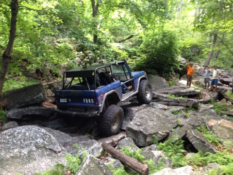 1988 Ford Bronco - This blue 1988 Ford Bronco, equipped with a roll cage, tackles a challenging rocky terrain on an off-road trail.