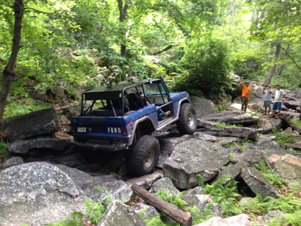 Blue 1988 Ford Bronco navigating a rocky off-road trail with a roll cage