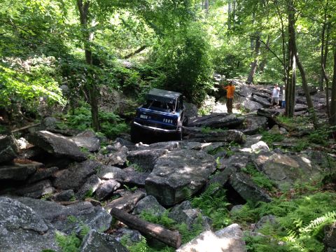 1988 Ford Bronco - Ford Bronco tackling a challenging off-road course filled with large rocks and dense foliage.