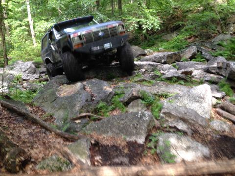 1988 Ford Bronco - A black Ford Bronco tackles a challenging rocky terrain, demonstrating its off-road capabilities.
