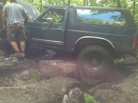 1988 Ford Bronco - A Ford Bronco is shown off-roading on a rocky trail with its hood up.
