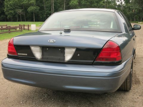 2001 Ford Crown Victoria - The rear of a blue 2001 Ford Crown Victoria is shown parked outdoors on a gravel surface.