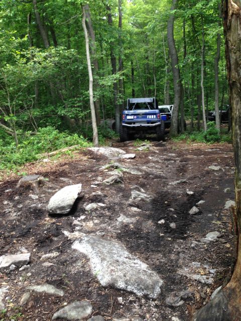 1988 Ford Bronco - A blue Ford Bronco is parked on a rough, wooded trail with another vehicle visible in the background.