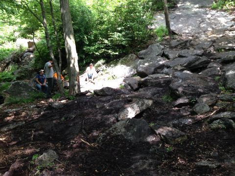 1988 Ford Bronco - Several people are resting on rocks in a forest clearing with a muddy trail.