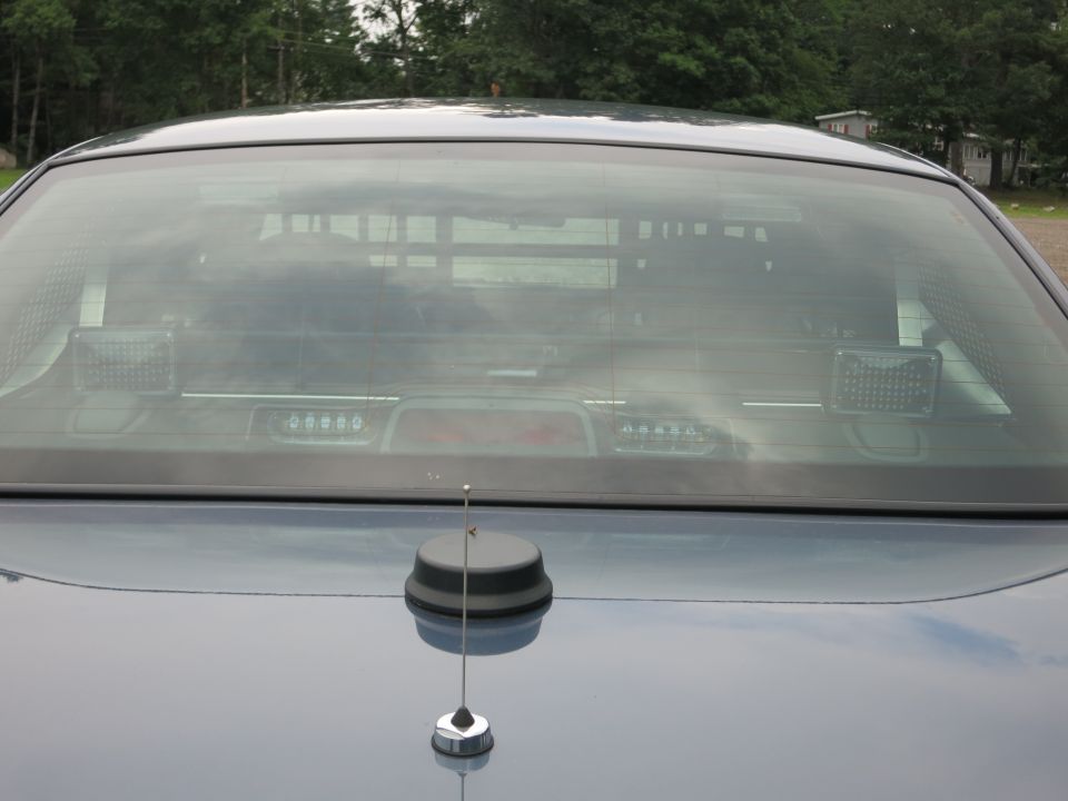 Rear window and trunk of a dark sedan with an antenna on the trunk