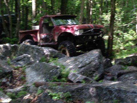 1988 Ford Bronco - Modified red pickup truck navigating a rocky trail in a wooded area.
