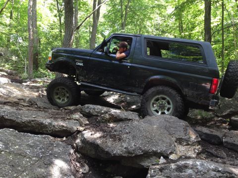 1988 Ford Bronco - A black 1988 Ford Bronco navigates a rocky trail, demonstrating its off-road capabilities.