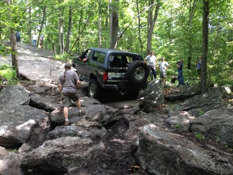 1988 Ford Bronco - A dark SUV navigates a challenging rocky terrain with onlookers present.