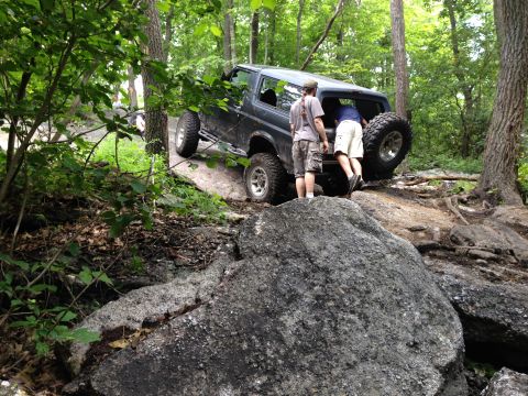 1988 Ford Bronco - A Ford Bronco tackles a challenging off-road course with two people observing.