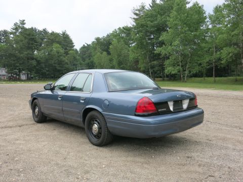 2001 Ford Crown Victoria - Rear view of a blue 2001 Ford Crown Victoria sedan on a gravel surface with trees in the background.