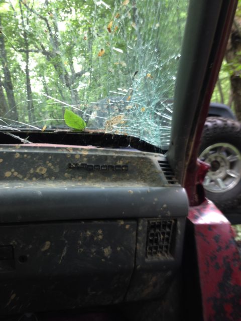 1988 Ford Bronco - The interior of a muddy off-road vehicle shows a severely cracked windshield and a glimpse of another vehicle outside.